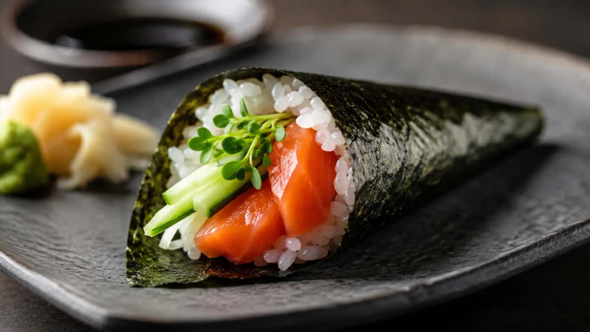 Handgjord japansk temaki-sushi med krispig nori, sashimi-lax och kaiware på träbricka