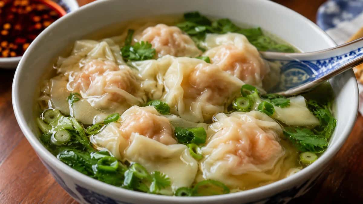 Kantonesiska wontons med räka och fläsk i het buljong med salladslök och koriander serverade i skål